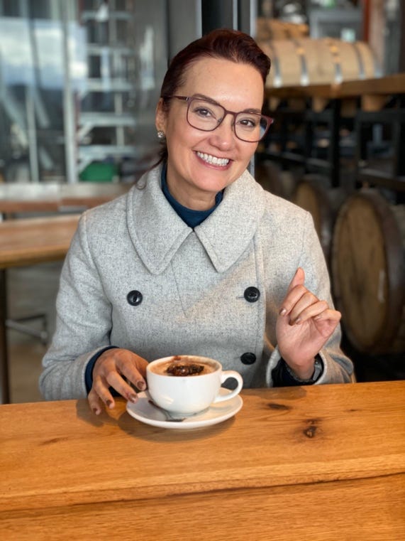 Photo of Christy Passion in a coat with a hand on a coffee on a table